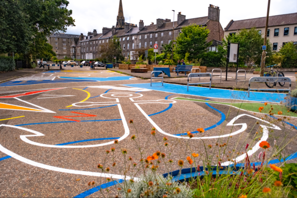 Bright display of new Leith ground art with view of bicycle parking and two adults sitting on a bench